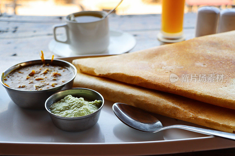 印度早餐masala dosa的图片，薄的折叠土豆煎饼放在白色盘子上，蘸酱/调味品/酸辣酱，包括萨姆巴，咖啡作为背景